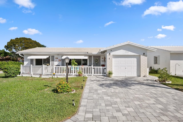 single story home with decorative driveway, brick siding, covered porch, a front yard, and a garage