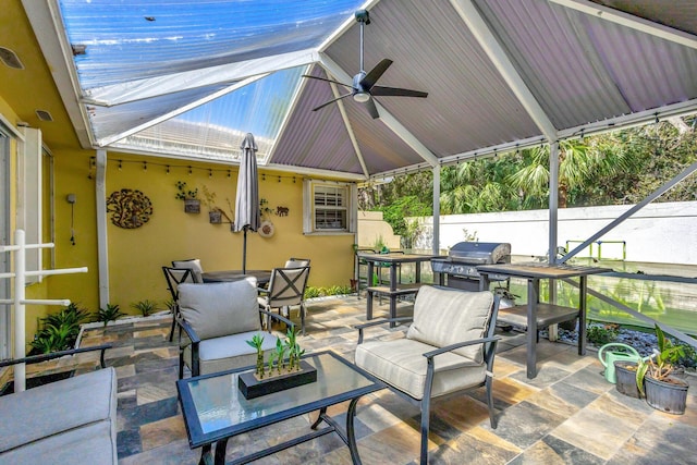 view of patio / terrace featuring ceiling fan, glass enclosure, fence, an outdoor living space, and grilling area