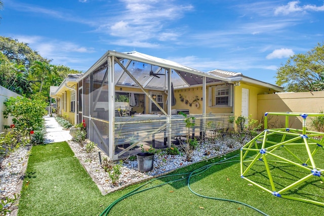 rear view of property with ceiling fan, a yard, fence, and stucco siding