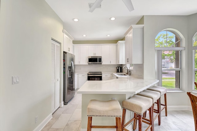 kitchen featuring a breakfast bar area, stainless steel appliances, backsplash, a sink, and a peninsula