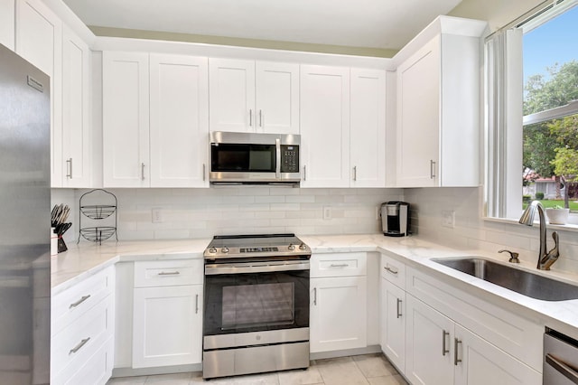 kitchen featuring a sink, white cabinets, appliances with stainless steel finishes, light stone countertops, and tasteful backsplash