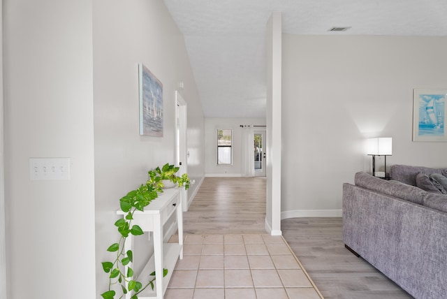 hall featuring lofted ceiling, light wood-style flooring, baseboards, and visible vents