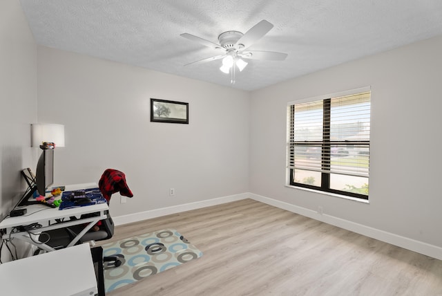 office space with baseboards, ceiling fan, a textured ceiling, and light wood-style floors