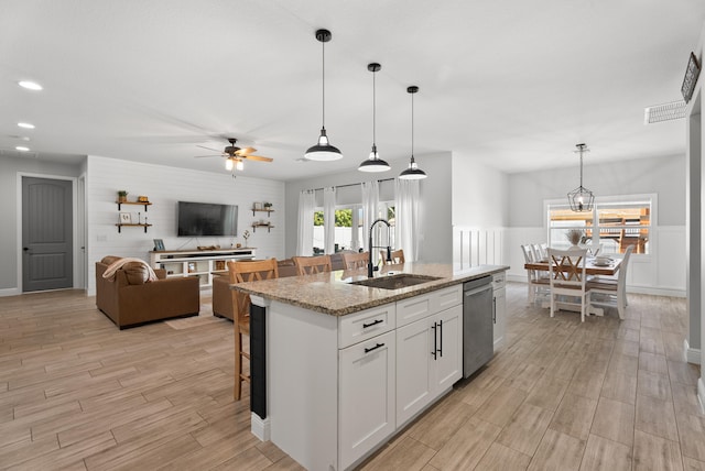 kitchen with wood finish floors, a center island with sink, dishwasher, white cabinetry, and a sink