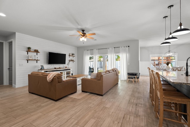 living area featuring light wood-style flooring, ceiling fan with notable chandelier, and a wainscoted wall