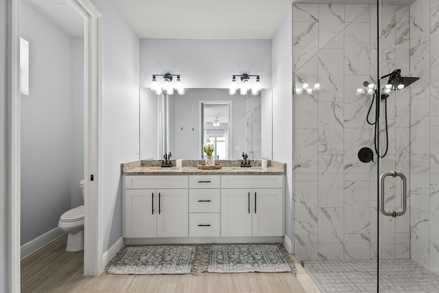 bathroom featuring a marble finish shower, double vanity, toilet, and a sink