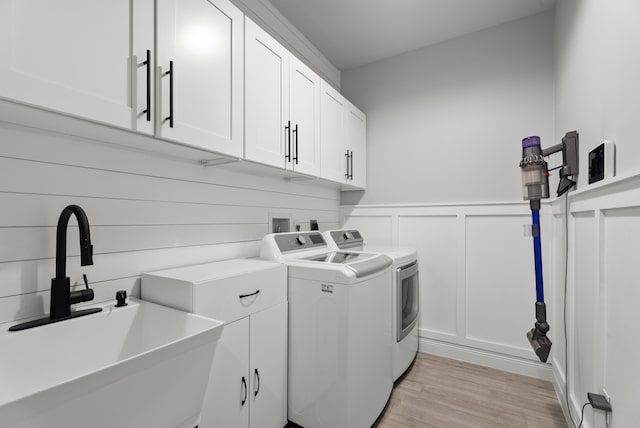 laundry room featuring cabinet space, separate washer and dryer, a sink, light wood-style floors, and a decorative wall