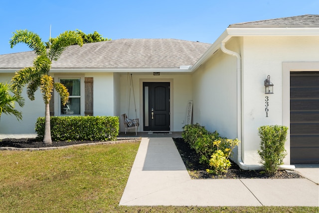 property entrance featuring a shingled roof, a lawn, a garage, and stucco siding