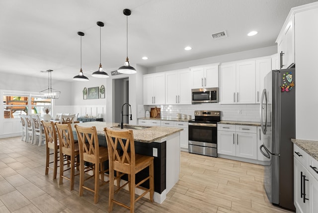 kitchen with visible vents, a sink, light stone counters, appliances with stainless steel finishes, and decorative backsplash