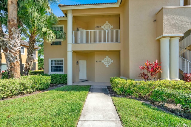 view of front of property with stucco siding, a front lawn, a tile roof, and a balcony