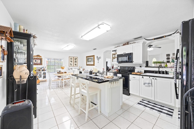 kitchen featuring light tile patterned floors, dark countertops, white cabinetry, a kitchen island, and black appliances