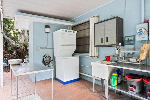 clothes washing area featuring a sink, laundry area, stacked washer / dryer, and light tile patterned flooring