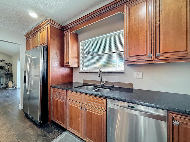 kitchen with brown cabinets, appliances with stainless steel finishes, a sink, a textured ceiling, and dark stone countertops