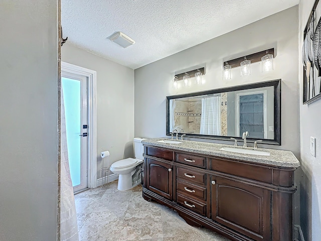 bathroom featuring a sink, a textured ceiling, toilet, and double vanity