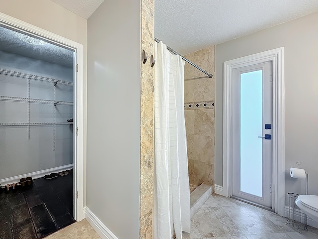 full bathroom featuring a textured ceiling, tiled shower, toilet, and baseboards