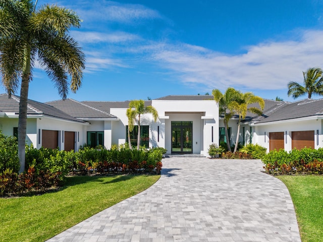 view of front of home featuring french doors, decorative driveway, a front yard, and stucco siding