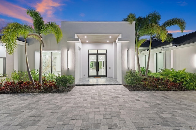 exterior entry at dusk featuring french doors and stucco siding