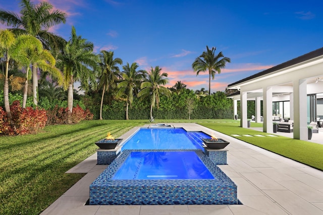 pool at dusk featuring a fenced in pool, a yard, an outdoor fire pit, a patio area, and an in ground hot tub