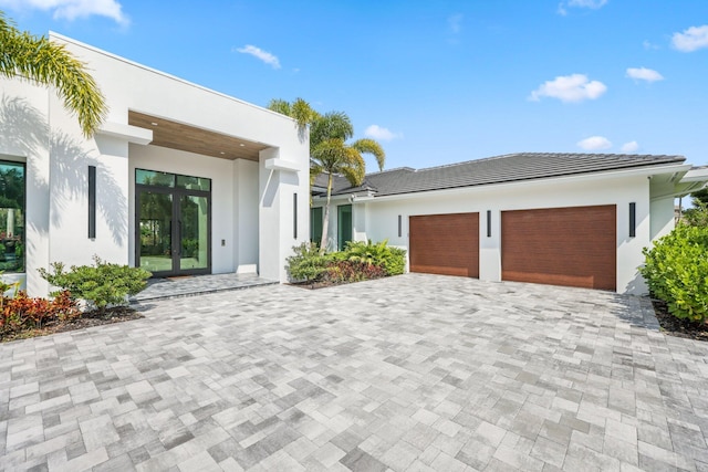 view of front facade featuring french doors, decorative driveway, an attached garage, and stucco siding