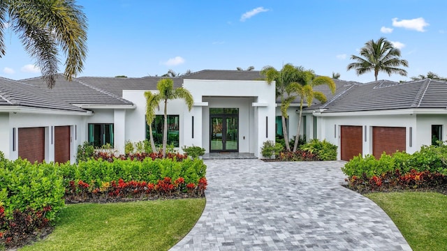 view of front of property with a tile roof, an attached garage, decorative driveway, a front lawn, and stucco siding