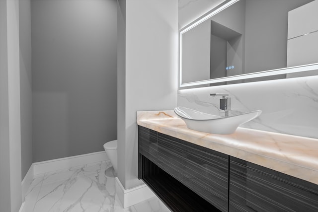 half bathroom featuring marble finish floor, toilet, vanity, and baseboards