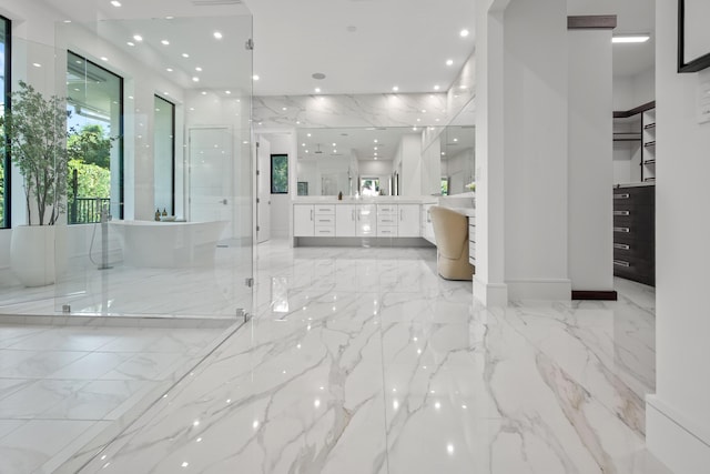 bathroom featuring a freestanding bath, marble finish floor, vanity, and stone wall