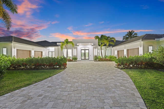 view of front of home with decorative driveway, french doors, a yard, and an attached garage