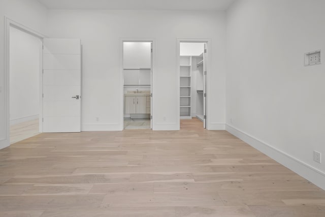 unfurnished bedroom with light wood finished floors, a spacious closet, and baseboards