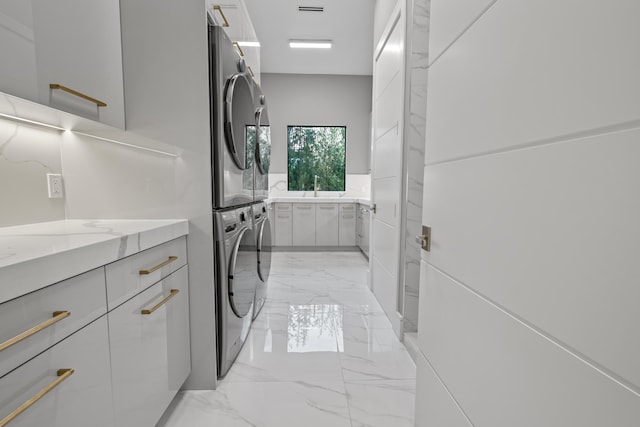 clothes washing area featuring marble finish floor, stacked washing maching and dryer, and laundry area