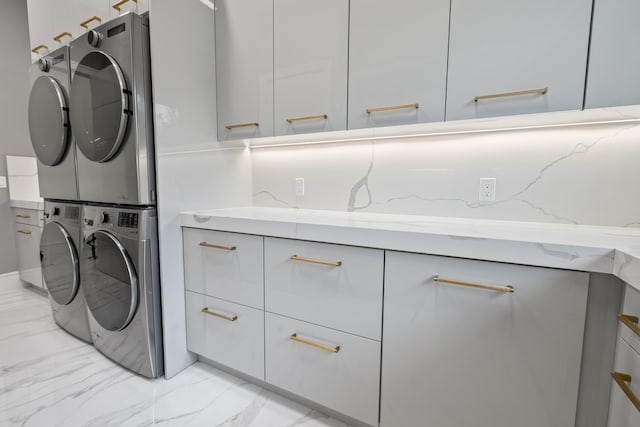 laundry area featuring marble finish floor, cabinet space, and stacked washer / dryer