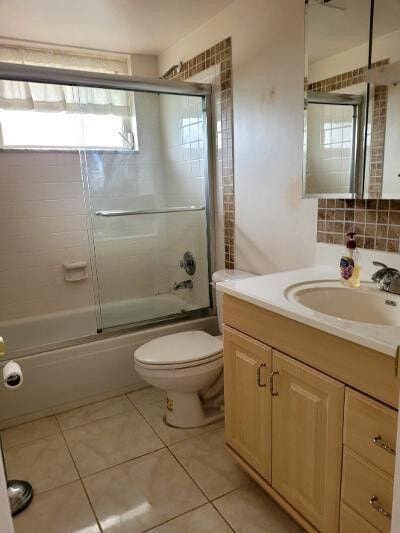 full bathroom with decorative backsplash, toilet, combined bath / shower with glass door, vanity, and tile patterned floors