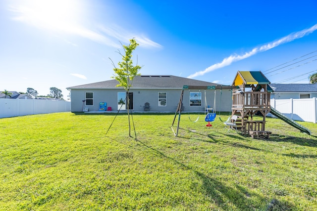 back of house with a playground, a yard, a fenced backyard, and stucco siding