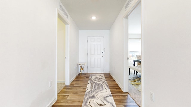 corridor with light wood-style flooring, visible vents, and baseboards