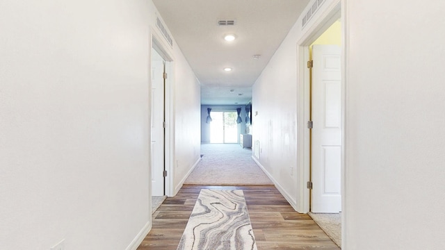 corridor featuring visible vents, light wood-style flooring, and baseboards