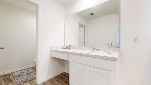 bathroom with baseboards, visible vents, toilet, wood finished floors, and vanity