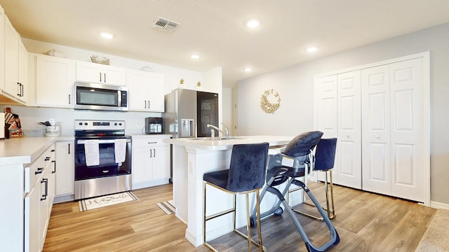 kitchen featuring stainless steel appliances, visible vents, light wood-style floors, light countertops, and a kitchen bar