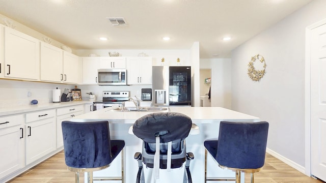 kitchen featuring a breakfast bar, light wood finished floors, visible vents, appliances with stainless steel finishes, and a sink