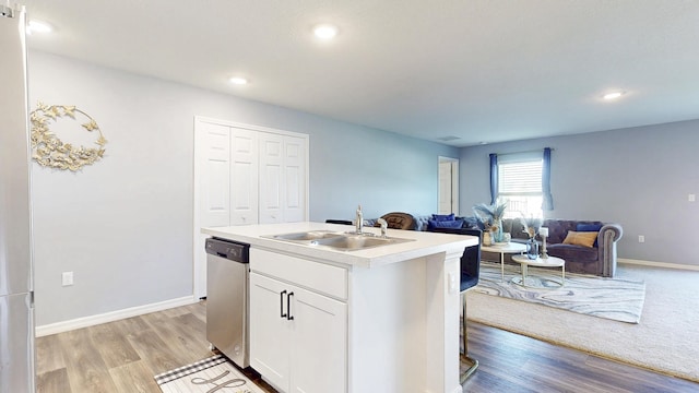 kitchen featuring light countertops, stainless steel dishwasher, open floor plan, white cabinets, and a sink