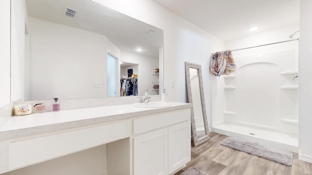 full bath featuring wood finished floors, vanity, visible vents, a stall shower, and a walk in closet