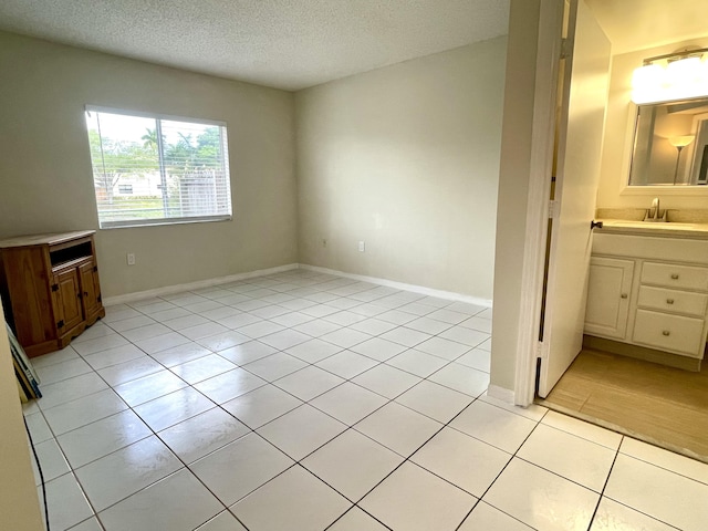 interior space featuring a sink, light tile patterned floors, baseboards, and a textured ceiling