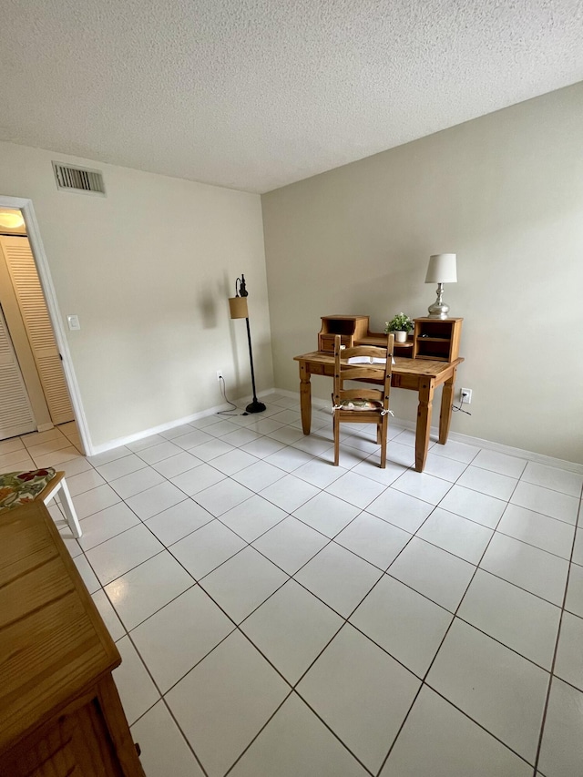 office featuring light tile patterned floors, a textured ceiling, visible vents, and baseboards