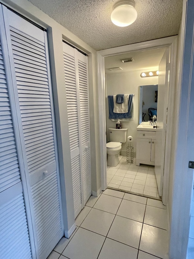 bathroom featuring a textured ceiling, toilet, vanity, a closet, and tile patterned floors