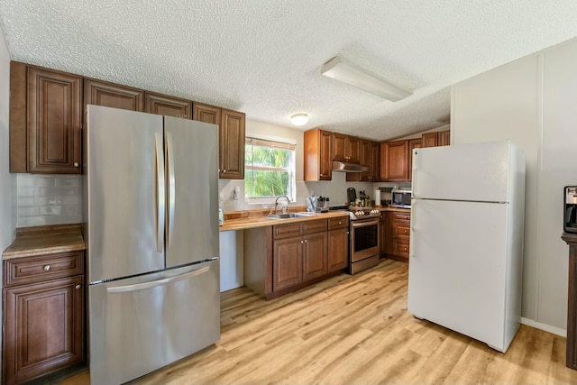 kitchen with decorative backsplash, appliances with stainless steel finishes, light wood-style floors, a sink, and under cabinet range hood