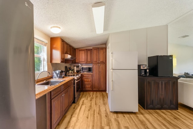 kitchen featuring appliances with stainless steel finishes, light wood-style floors, brown cabinetry, a sink, and under cabinet range hood