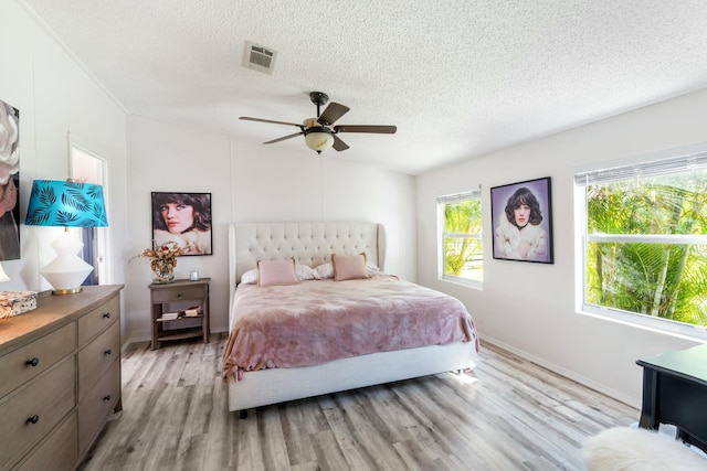 bedroom featuring a textured ceiling, ceiling fan, visible vents, and light wood-style floors