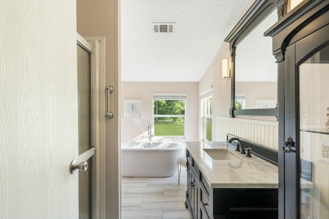 full bath featuring a textured ceiling, a freestanding tub, vanity, visible vents, and a shower stall