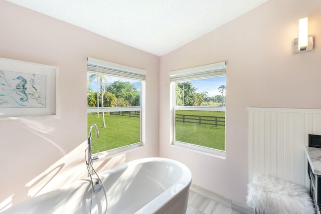 bathroom with vaulted ceiling, a freestanding bath, a textured ceiling, and baseboards