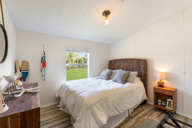 bedroom with lofted ceiling, a textured ceiling, baseboards, and wood finished floors