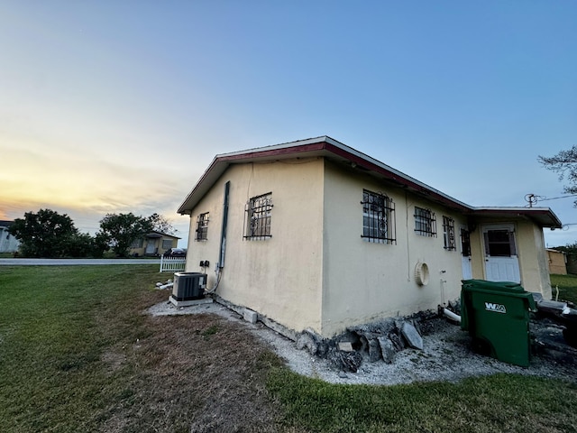 property exterior at dusk featuring central AC unit, a lawn, and stucco siding