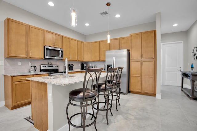 kitchen with visible vents, light stone counters, a kitchen island with sink, stainless steel appliances, and backsplash